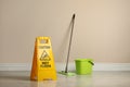 Safety sign with phrase Caution wet floor, mop and bucket indoors. Cleaning service Royalty Free Stock Photo