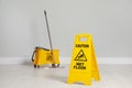 Safety sign with phrase Caution wet floor, mop and bucket indoors. Cleaning service Royalty Free Stock Photo