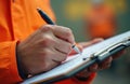 Safety supervisor in orange jacket writes on clipboard at work site. Inspector taking notes for report during check. Male hand Royalty Free Stock Photo