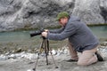 A photographer adjusting his camera on a stand with both hands to take photo of Rhine whitewater.