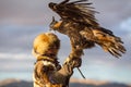 Young Kazakh Eagle Huntress Berkutchi woman with horse while hunting to the hare with a golden eagles on his arms