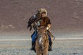 Young Kazakh Eagle Huntress Berkutchi woman with horse while hunting to the hare with a golden eagles on his arms Royalty Free Stock Photo