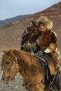 Young Kazakh Eagle Huntress Berkutchi woman with horse while hunting to the hare with a golden eagles on his arms