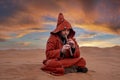 Man in traditional red clothes playing flute while sitting on sand in desert