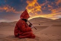 Man in traditional red clothes playing flute while sitting on sand in desert