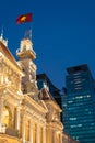 Saigon City Hall People`s Committee Head office with waving Vietnamese flag and Vincom Center towers in the background at night