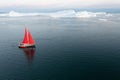 Sail boat with red sails cruising among ice bergs during dusk in front of a full moon. Royalty Free Stock Photo