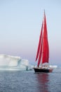 Sail Boat With Red Sails Cruising Among Ice Bergs During Sunrise. Disko Bay, Greenland.