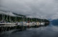 Sail, yachts and motor boats anchor in the harbor. Calm water and the green misty mountains after rain. Deep Cove