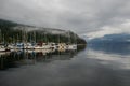 Sail, yachts and motor boats anchor in the harbor. Calm water and the green misty mountains after rain. Deep Cove