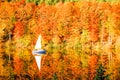 a sailboat and an autumn forest of red yellow and green autumn colors are reflected in the lake surface Royalty Free Stock Photo