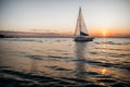 A sailboat bobbing on the horizon at sunset