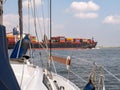 Sailboat crossing Westerschelde in the Netherlands, waiting for container ship to Antwerp, Belgium Royalty Free Stock Photo