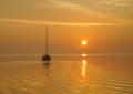 A sailboat departs a quiet anchorage into a bright yellow sunrise