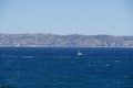 Sailboat gliding across a sparkling blue sea with mountains and a blue sky in the background