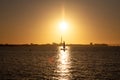 A sailboat and a man standing on a surf board is meeting on the sea as silhouettes as the sun sets over MalmÃÂ¶, Sweden