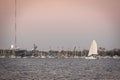 A sailboat on the open water passing a harbor with other boats docked Royalty Free Stock Photo