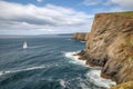 sailboat rounding the point, with dramatic cliff and ocean in the background