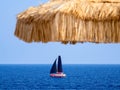 Sailboat on the sea and a straw parasol