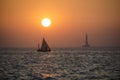 A sailboat in the sea during sunset with a lighthouse in the background