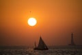A sailboat in the sea during sunset with a lighthouse in the background Royalty Free Stock Photo