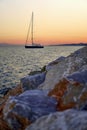 Sailboat on the sea at sunset, rocks in foreground