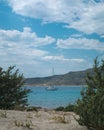 Sailboat seen from between green bushes on in Elafonisos, Greece on a beautiful day with blue sky and clouds. Simos beach.