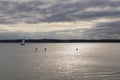 Sailboat on tranquil waters with people paddleboarding on background of the sunset sky Royalty Free Stock Photo