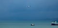 Sailboat traversing the tranquil ocean waters with an airplane soaring in the sky above it.