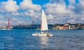 Sailboat with white sails on Tagus River, 25 of April Bridge, Christ the king elevator tower in the background,  near Lisbon. Royalty Free Stock Photo