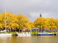 Sailboats at jetty in marina, trees in autumn colours and storm clouds, Enkhuizen, Netherlands