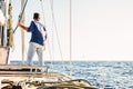 Sailing activity people - man viewed from back stand up on the deck of a sail boat looking horizon and blue ocean and sky