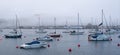 Sailing boats on a misty estuary. Early morning fog sits over calm water with sailboats and red Buoys in the foreground. Royalty Free Stock Photo