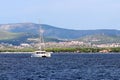 Sailing catamaran sails along the rocky green coast past the red literary sign - the fairway lighthouse. City of Sibenik in the Da