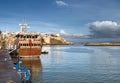 Sailing ship near the pier and the boat (even with the fishermen) on the background of the old fortress and buildings made of whit