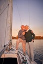 Sailing at sunset. Full length of happy senior couple holding hands and hugging while standing on the side of yacht deck Royalty Free Stock Photo