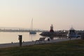 The sailing yacht enters under the motor in the marina in the rays of the morning sun. Dawn in the port. Empty bench on the pier