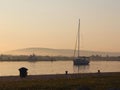 The sailing yacht enters under the motor in the marina in the rays of the morning sun. Dawn in the port. Empty pier with electrica