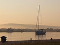 The sailing yacht enters under the motor in the marina in the rays of the morning sun. Dawn in the port. Empty pier with