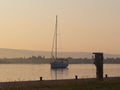 The sailing yacht enters under the motor in the marina in the rays of the morning sun. Dawn in the port. Empty pier with