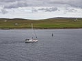 A Sailing Yacht with its sail stowed motors towards the Town of Lerwick with Bressay in the background. .