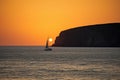 sailing yacht rounding headland, with the sun setting in the background