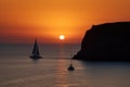 sailing yacht rounding headland, with the sun setting in the background