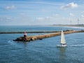 Sailing yacht setting out to sea on a sunny day passing the breakwater and lighthouse Royalty Free Stock Photo