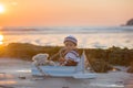 Sailor baby boy, cute child, playing on the beach with wooden boat, fishes and fishing rod on sunset Royalty Free Stock Photo