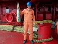 Sailor in uniform shows his lucky catch - big fish caught in ocean from ship deck of oil tanker Royalty Free Stock Photo