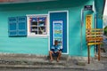 Senior man sits next to the mini market shop entrance in Fond de Rond Point in Saint-Denis De La Reunion, France.