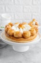 Saint Honore cake with profitrols, caramel, custard and whipped cream on a white plate on a gray concrete background.