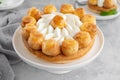 Saint Honore cake with profitrols, caramel, custard and whipped cream on a white plate on a gray concrete background.