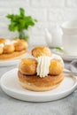 Saint Honore cake with profitrols, caramel, custard and whipped cream on a white plate on a gray concrete background.